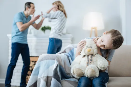 My best friend. Unhappy fair-haired little girl holding a teddy bear and sitting on the sofa while her parents shouting at each other.