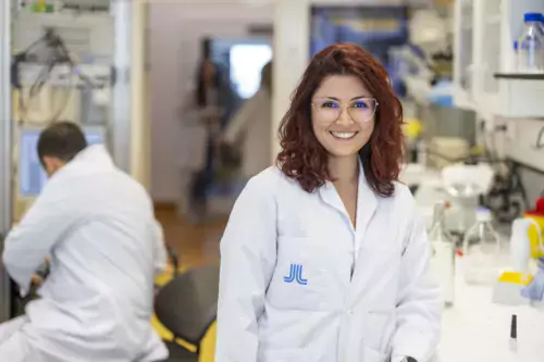 Woman in lab coat looking in to the camera smiling.