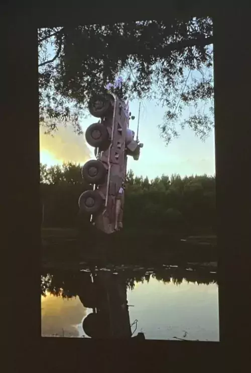 A tank hanging upside-down, being fished out of a lake
