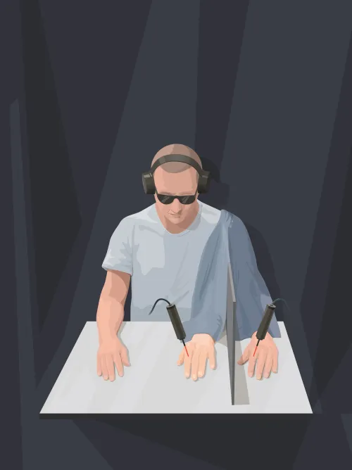 Person wearing headphones and dark glasses and both hands are presented. The left hand is hidden behind a screen, but a prosthetic left hand is exposed to stimuli.