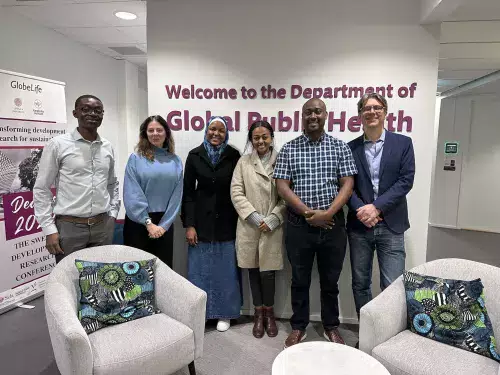 Researchers on exchange to Karolinska Institutet within the HoliCare project, group picture of the three researchers from Africa and KI in front of the sign welcome to the Department of Global Public Health.