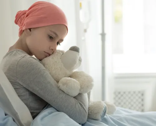 A child with cancer is sitting on a hospital bed