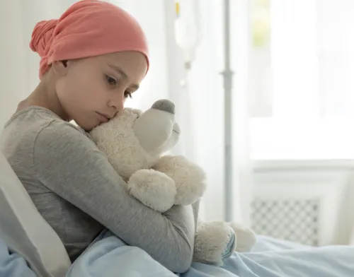 A child with cancer is sitting on a hospital bed