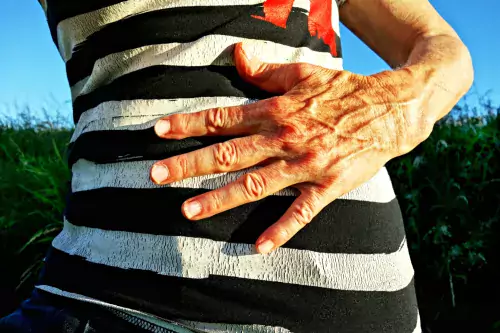 Elderly woman holds her hand over her belly. She is dressed in a striped sweater.