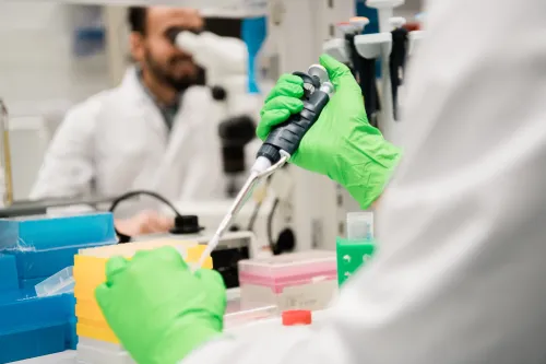 A person pipetting with green gloves on.
