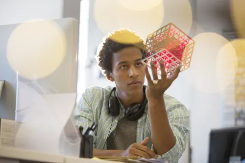 A young man in deep thought. He is looking at a cube that he is holding in his hand.