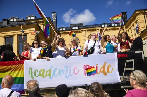 A group of people on a truck with the words ‘academic pride’ waving rainbow flags.