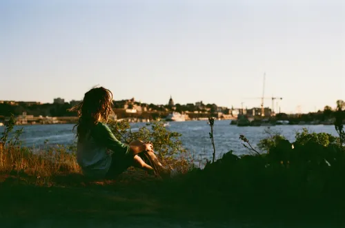 Young person sitting on a mountain ridge in Stockholm, looking out over the water and the city.