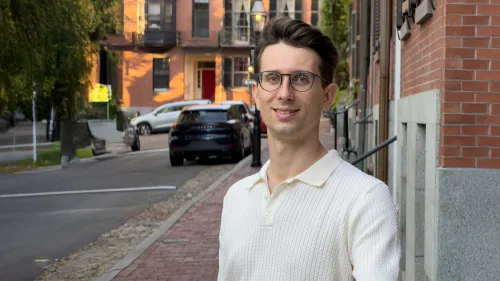 Tilen Trselic standing on a street in a city, surrounded by houses and parked cars. Tilen looks straight into the camera and smiles.