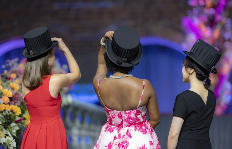 Three women facing away from the camera lift their doctoral hats.
