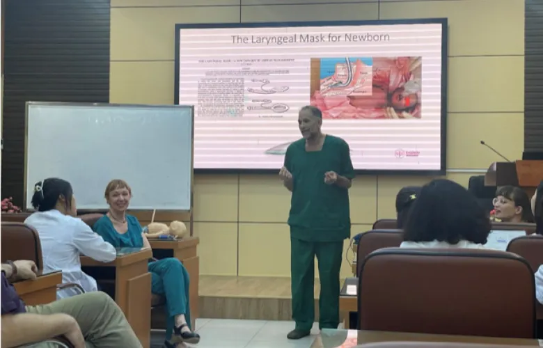 Susanna Myrnets Höök and Nicolas Pejovic presenting upcoming studies to the Neonatal Department at Phu San Hospital in front of projector screen wearing green hospital clothes.